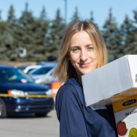 GVSU Alumna smiles as she carries a stack of 3 boxes